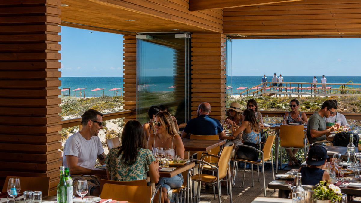 Clientes almoçando no deck panorâmico de madeira do restaurante Estaminé com vista para o mar da Ilha Deserta em Faro.